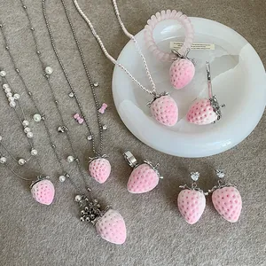 Rosa beflocktes Erdbeer-Schmuckset mit Halsketten, Ohrringen und Ringen auf strukturiertem Grund