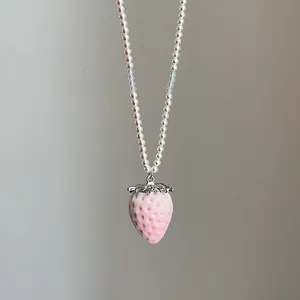 Detail eines rosa Erdbeeranhängers mit Textur an einer weißen Perlenkette für Damen