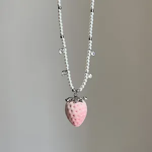 Detail der rosa beflockten Erdbeere an einer weißen Perlenkette mit silbernen Herzakzenten