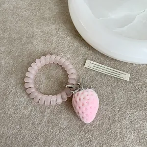 Nahaufnahme des rosa beflockten Erdbeeranhängers an einem transparenten Spiralhaargummi