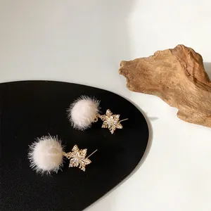Winter snowflake earrings with beige faux fur pom poms and zircon accents on black texture