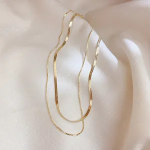Collier double couche doré avec chaîne serpent et chaîne fine sur tissu crème