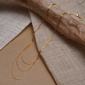 Détail d'un collier triple couche doré avec chaînes fines et breloque cœur