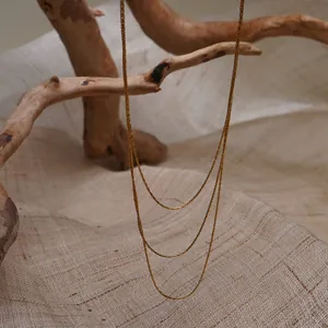 Détail d'un collier à plusieurs rangs en maille serpent dorée drapé sur du bois