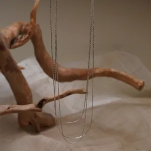 Détail d'un collier chaîne argentée à plusieurs rangs suspendu sur du bois naturel