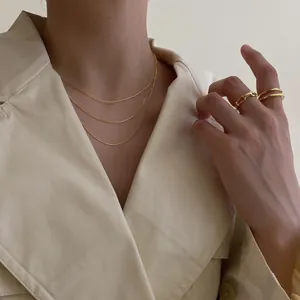 Détail d'un collier à chaînes dorées et de bagues portées sur un manteau beige