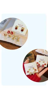 Close-up showing red Chinese knot lucky cat and fortune bag stud earrings on display card