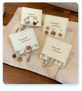Detalle de juegos de pendientes de gato y oso con perlas sobre fondo de tela suave