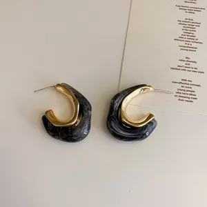 Detail view of French retro gold metal and black marbled resin geometric hoop earrings.