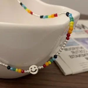 Détail d'un collier de perles colorées avec pendentif smiley argenté sur bol en céramique