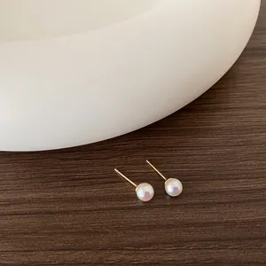Dettaglio di orecchini di perle minimalisti con perni dorati su legno scuro