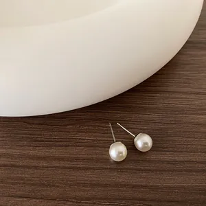 Dettaglio di orecchini con perle bianche minimalisti su sfondo di legno marrone