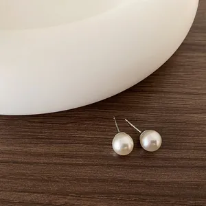 Dettaglio macro di orecchini a perno con perla bianca 8mm su sfondo in legno di noce scuro