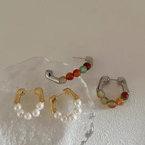 Elegant U-shaped hoop earrings with pearls and colorful stones on a textured surface
