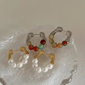 Minimalist U-shaped metal earrings set with natural stones and white pearls on glass tray