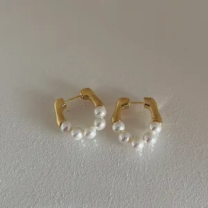 Close-up of gold metal hoop earrings with five white pearls on light grey background