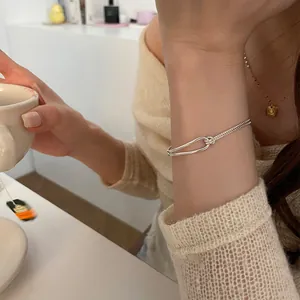 Minimalist silver double-layer knotted bracelet worn while holding a coffee cup