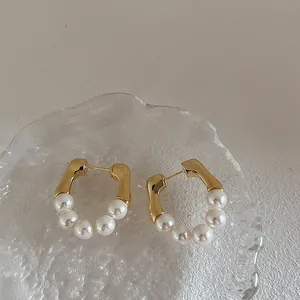 Macro detail of gold U-shaped earrings featuring five elegant white pearls on a glass tray