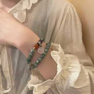 Close-up of a double-layer green beaded bracelet with a teardrop pendant on a wrist