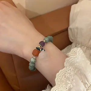 Detail of beaded bracelet with green stones and a white gourd pendant on a woman wrist