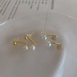 Detailed close-up of gold-plated freshwater pearl and zircon earrings in a tray