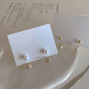 Detail of 925 silver needle pearl earrings with cubic zirconia charms on white display card