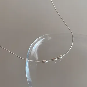 Détail du collier chaîne serpent argentée avec trois perles ovales sur décor en verre