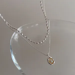 Détail d'un collier double rang argenté avec pendentif irrégulier et perle lustrée