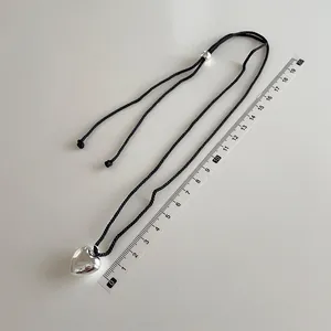 Long braided cord necklace with silver heart pendant and measuring ruler for size scale