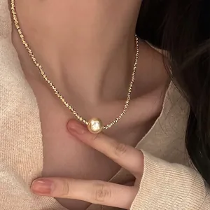 Detail einer goldenen gedrehten Kette mit einem glänzenden Perlenanhänger im Vintage-Stil