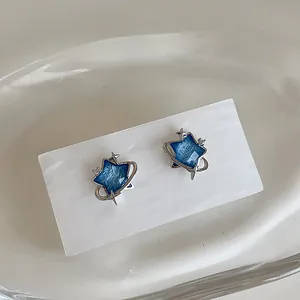 Detail shot of silver star-shaped earrings with blue zircon and saturn ring design