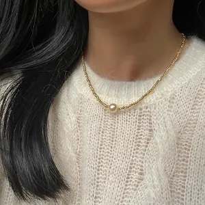 Detail einer minimalistischen Goldperlenkette mit großer Mittelperle auf weißem Strick