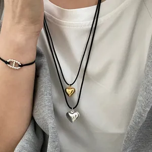 Close-up of gold and silver heart pendants on black woven cords with link bracelet