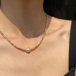 Detailaufnahme einer goldenen Perlenkette mit einem zentralen glänzenden Perlenanhänger