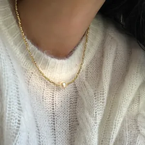 Detail einer goldenen Perlenkette mit einer einzelnen Perle auf einem weißen Strickpullover