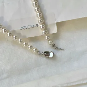 Détail d'un collier de perles en verre blanc avec fermoir en métal argenté sur papier blanc