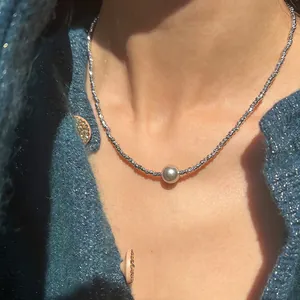 Detailansicht einer gedrehten Metallkette mit grauer Perle auf einem Strickpullover