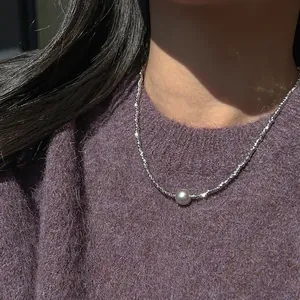 Silberne Perlenkette mit grauem Perlenanhänger auf lila Strickpullover-Hintergrund