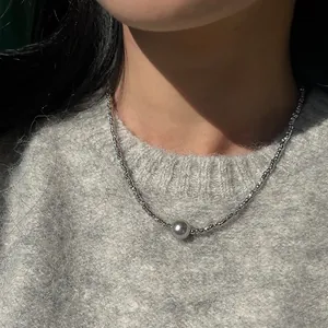 Nahaufnahme einer silbernen Halskette mit einer dunkelgrauen Perle im minimalistischen Stil