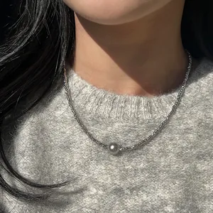 Nahaufnahme einer silbernen Halskette mit Metallic-Perlenanhänger auf einem Strickpullover