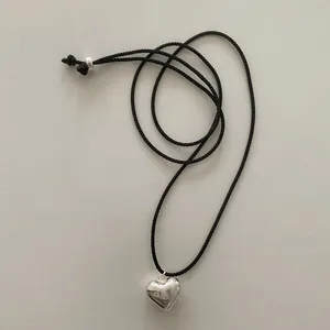 Close-up of polished silver heart pendant on a minimalist black woven cord necklace