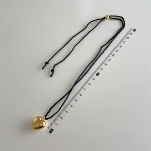 Detailed close-up of a gold heart pendant on a black woven cord with measuring ruler