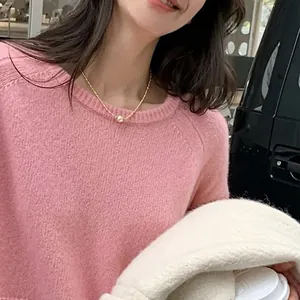 Nahaufnahme einer zarten Goldperlenkette auf einem rosa Strickpullover bei Tageslicht