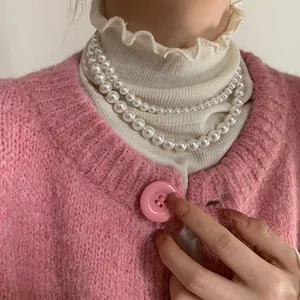 Détail du collier de perles blanches double couche porté avec un cardigan vintage