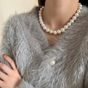 Gros plan d'un grand collier de perles blanches porté avec un pull gris sur le mannequin