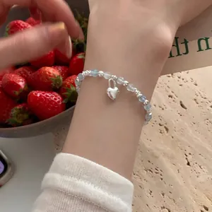 Detail of light blue beaded bracelet with silver heart charm on female wrist
