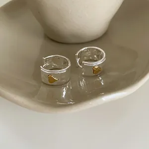 Detail of silver hammered wide hoop earrings featuring a gold heart accent on ceramic