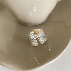 Macro detail of wide silver hammer-textured ring featuring a 3D gold heart accent