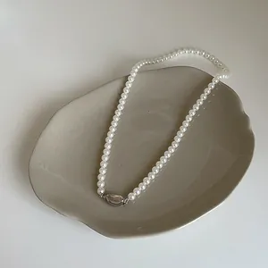 Gros plan du collier élégant en perles de verre blanches avec pendentif argenté sur plateau