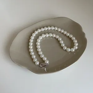 Gros plan d'un collier de perles blanches avec fermoir argenté sur plateau céramique